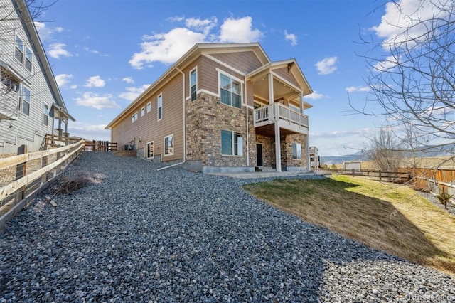 rear view of property featuring a patio area, stone siding, a fenced backyard, and a balcony