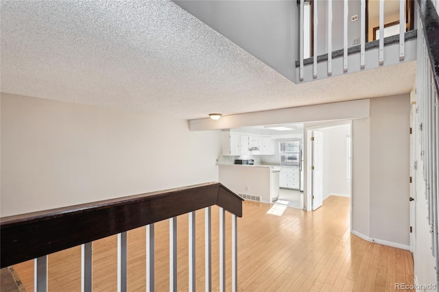 hall featuring visible vents, baseboards, a textured ceiling, and light wood-style flooring