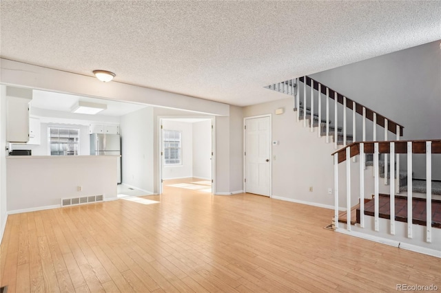 unfurnished living room with stairway, baseboards, visible vents, light wood-style flooring, and a textured ceiling