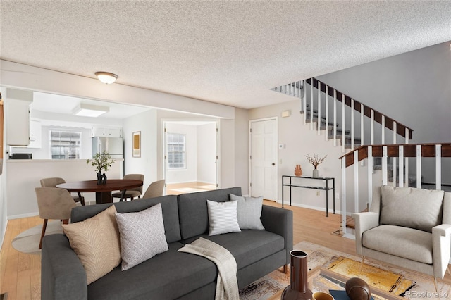 living room with stairs, baseboards, light wood-type flooring, and a textured ceiling