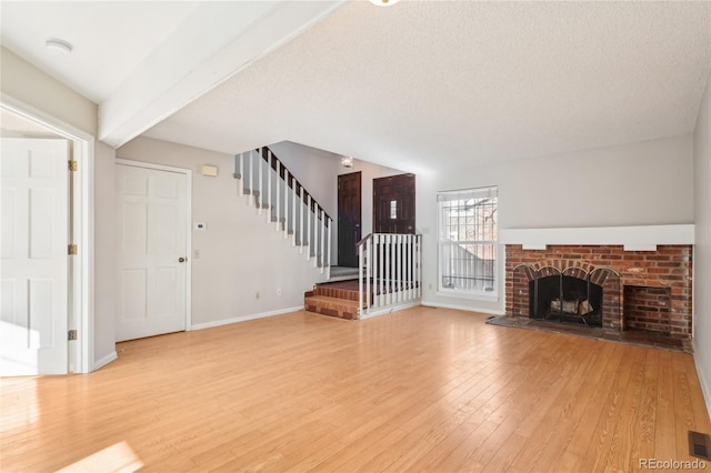 unfurnished living room featuring visible vents, baseboards, stairway, light wood-type flooring, and beam ceiling