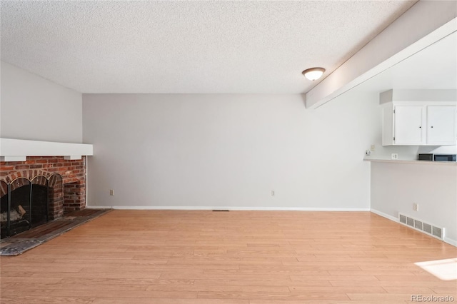 unfurnished living room featuring a textured ceiling, a brick fireplace, visible vents, and light wood-type flooring