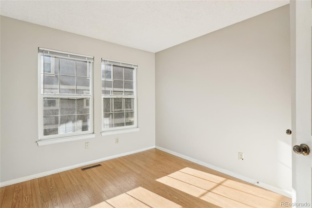 empty room featuring a textured ceiling, wood finished floors, visible vents, and baseboards