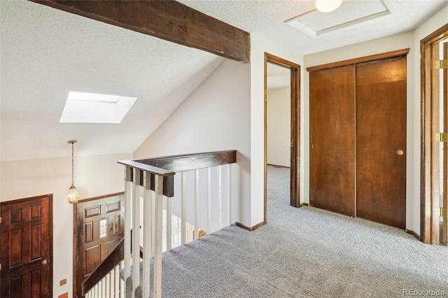 hallway with lofted ceiling with skylight, a textured ceiling, carpet floors, and an upstairs landing