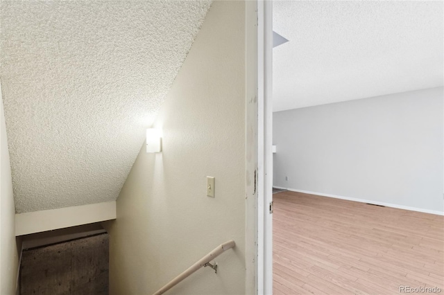 stairway with a textured ceiling, baseboards, and wood finished floors