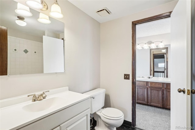 bathroom featuring toilet, a tile shower, a sink, two vanities, and visible vents