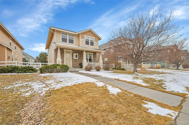 view of front of home with a porch, stone siding, and fence