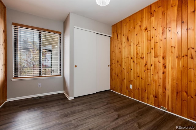 unfurnished bedroom with dark hardwood / wood-style flooring, wood walls, and a closet