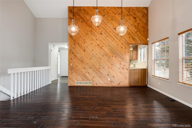 unfurnished living room with high vaulted ceiling, dark hardwood / wood-style flooring, wood walls, and sink