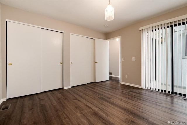 unfurnished bedroom with dark hardwood / wood-style flooring and multiple closets