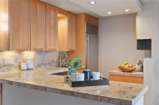 kitchen featuring light stone countertops, a peninsula, recessed lighting, built in refrigerator, and tasteful backsplash