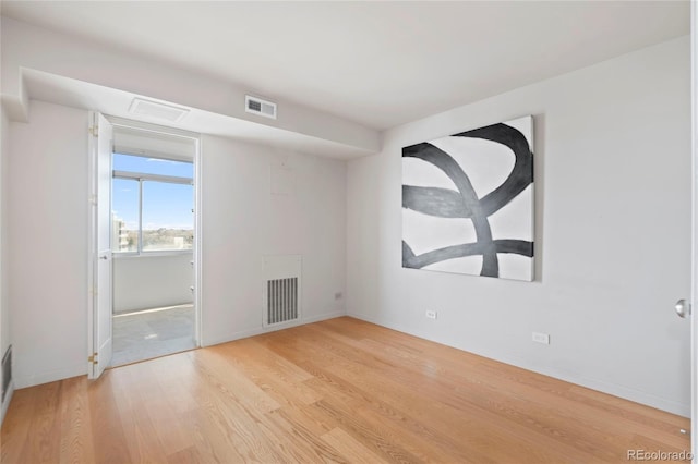 empty room featuring wood finished floors, visible vents, and baseboards