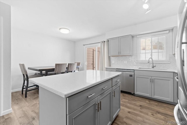 kitchen with a kitchen island, appliances with stainless steel finishes, hardwood / wood-style floors, sink, and gray cabinetry