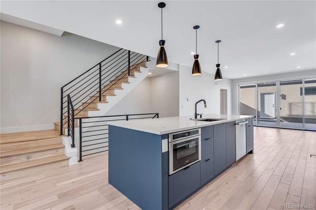 kitchen with sink, decorative light fixtures, a center island with sink, stainless steel appliances, and light hardwood / wood-style floors