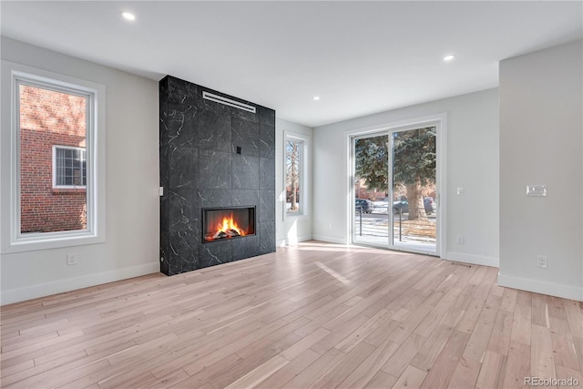 unfurnished living room with a healthy amount of sunlight, a high end fireplace, and light wood-type flooring