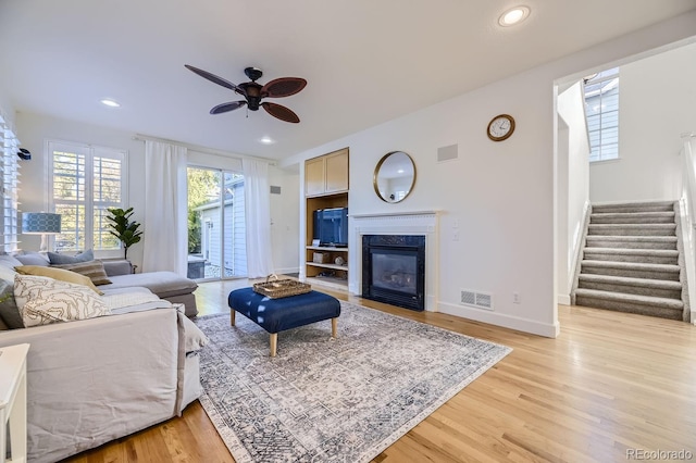 living room with a fireplace, ceiling fan, and light wood-type flooring