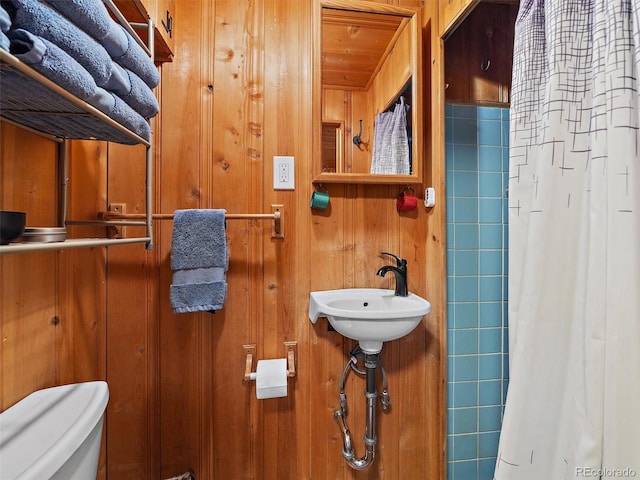 bathroom with wooden walls, sink, walk in shower, and toilet