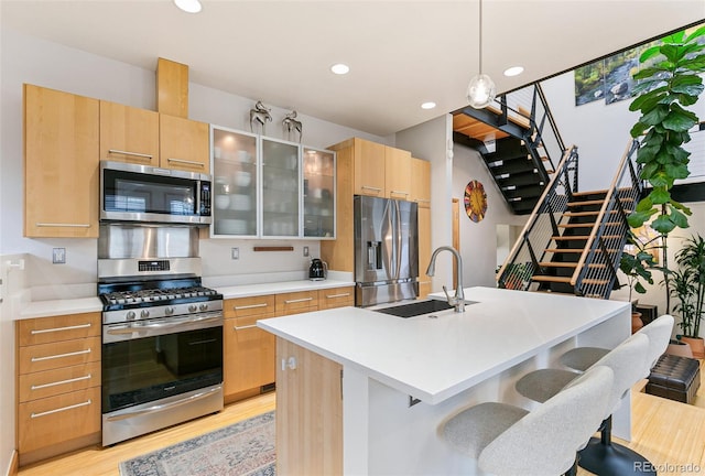 kitchen featuring pendant lighting, a center island with sink, sink, light brown cabinetry, and appliances with stainless steel finishes