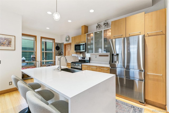 kitchen featuring hanging light fixtures, sink, stainless steel appliances, and a kitchen island with sink