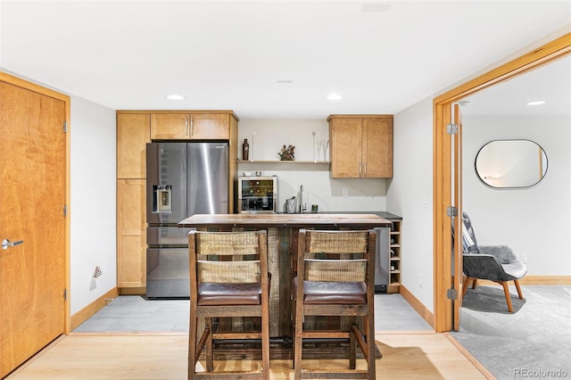 kitchen with a kitchen bar, stainless steel fridge with ice dispenser, and light hardwood / wood-style floors