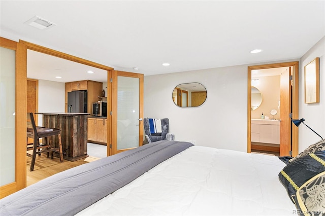 bedroom with refrigerator with ice dispenser, light wood-type flooring, indoor bar, and ensuite bath