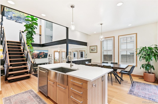 kitchen featuring pendant lighting, light brown cabinets, sink, light wood-type flooring, and an island with sink