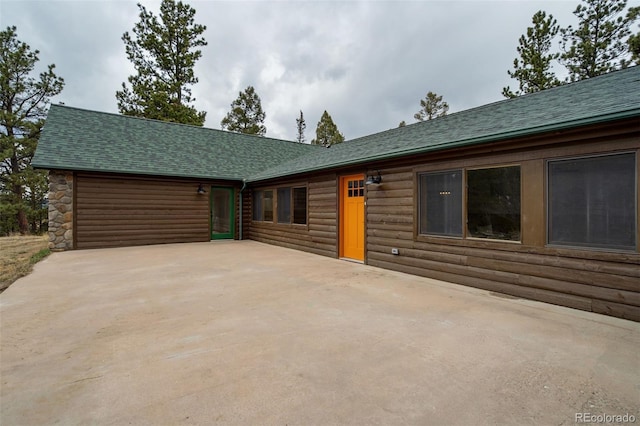 view of front of house with a shingled roof, a patio area, and log veneer siding