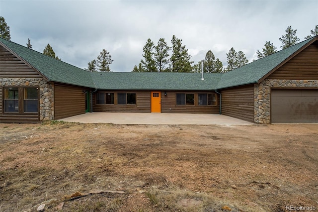 view of front facade featuring a shingled roof, a patio area, and faux log siding