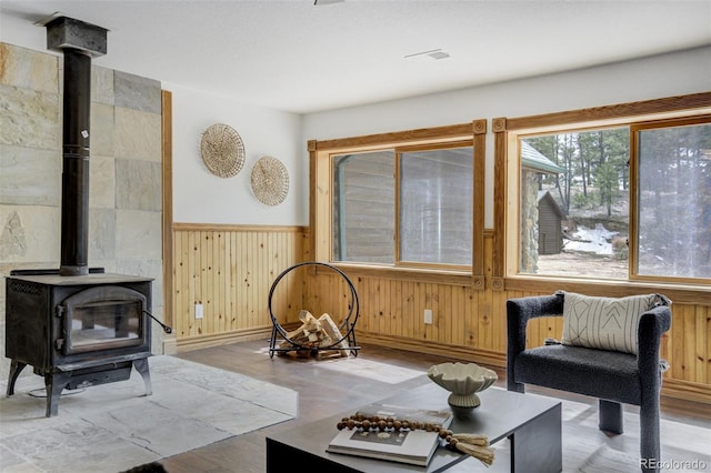 living room featuring wooden walls, a wood stove, a wainscoted wall, baseboards, and wood finished floors