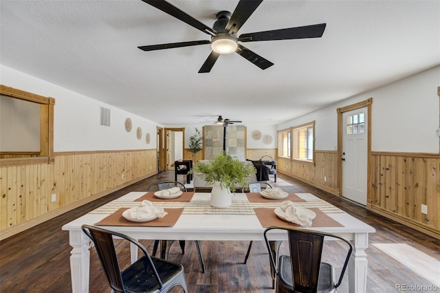 dining space with a wainscoted wall, a ceiling fan, wood walls, and wood finished floors