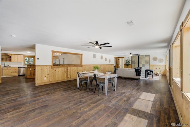 dining area featuring ceiling fan, wainscoting, a wood stove, and dark wood-type flooring