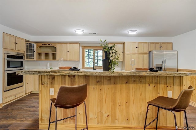 kitchen with light brown cabinetry, stainless steel appliances, and a kitchen bar
