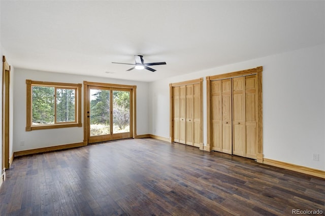 unfurnished bedroom featuring baseboards, access to exterior, multiple closets, and dark wood-type flooring