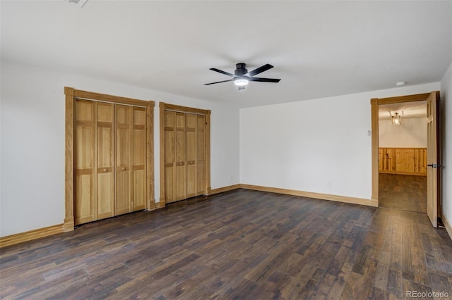 unfurnished bedroom with multiple closets, baseboards, and dark wood-style flooring