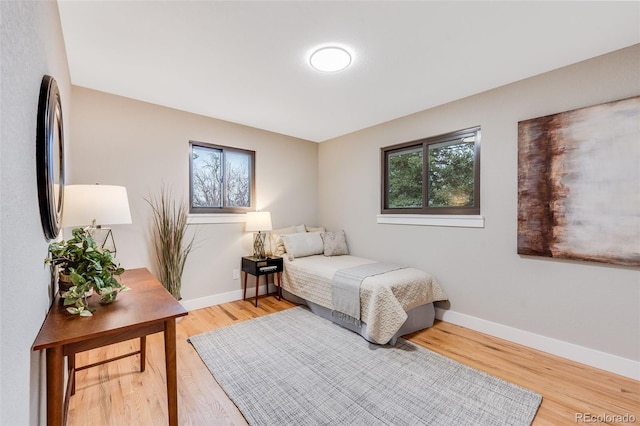 bedroom with multiple windows, light wood-type flooring, and baseboards