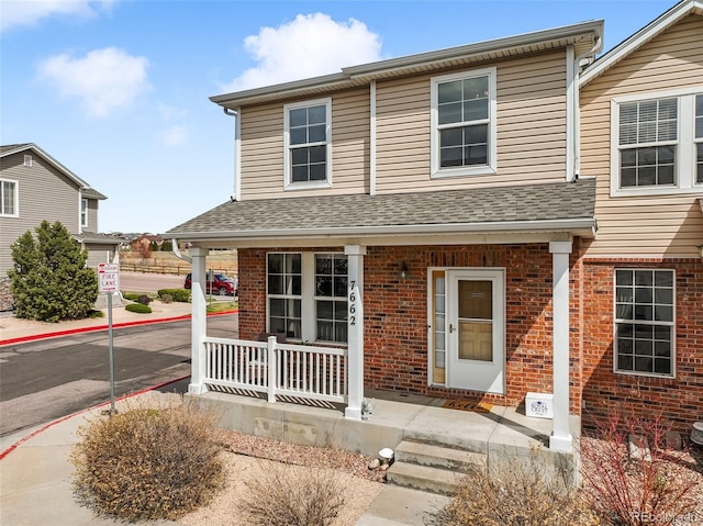view of front of home with a porch, a shingled roof, and brick siding
