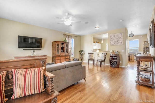 living room featuring ceiling fan, light wood finished floors, and baseboards
