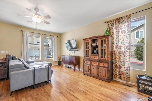 living room with light wood-type flooring, baseboards, a ceiling fan, and visible vents
