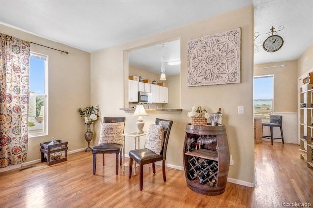 living area featuring visible vents, light wood-style flooring, baseboards, and a healthy amount of sunlight