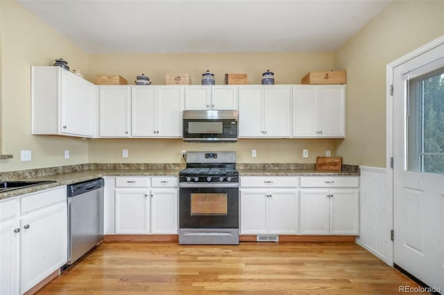 kitchen featuring light wood-style flooring, white cabinetry, wainscoting, visible vents, and appliances with stainless steel finishes