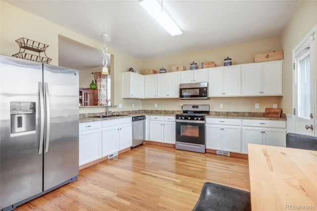 kitchen with light wood-style flooring, white cabinets, visible vents, stainless steel appliances, and a sink