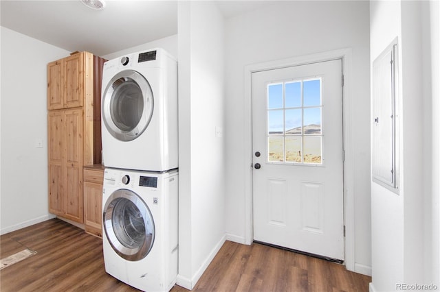 laundry room with stacked washer and dryer, dark hardwood / wood-style floors, and cabinets