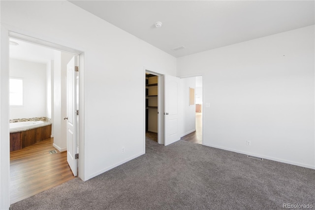 unfurnished bedroom with connected bathroom, dark carpet, a walk in closet, and a closet