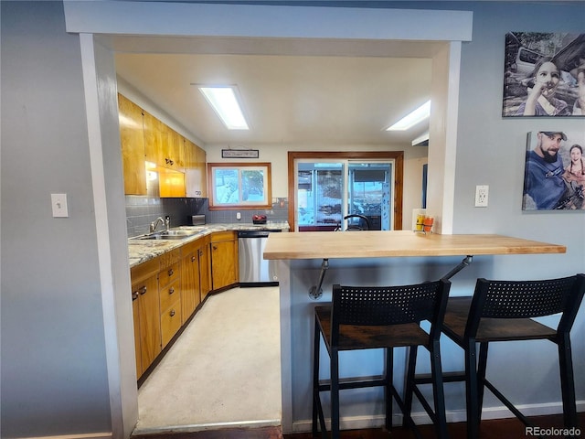 kitchen featuring sink, stainless steel dishwasher, tasteful backsplash, a kitchen bar, and kitchen peninsula