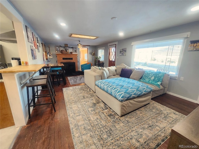 living room with ceiling fan, dark hardwood / wood-style flooring, and a brick fireplace