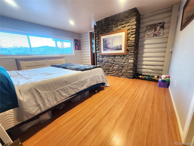 bedroom with log walls and hardwood / wood-style flooring