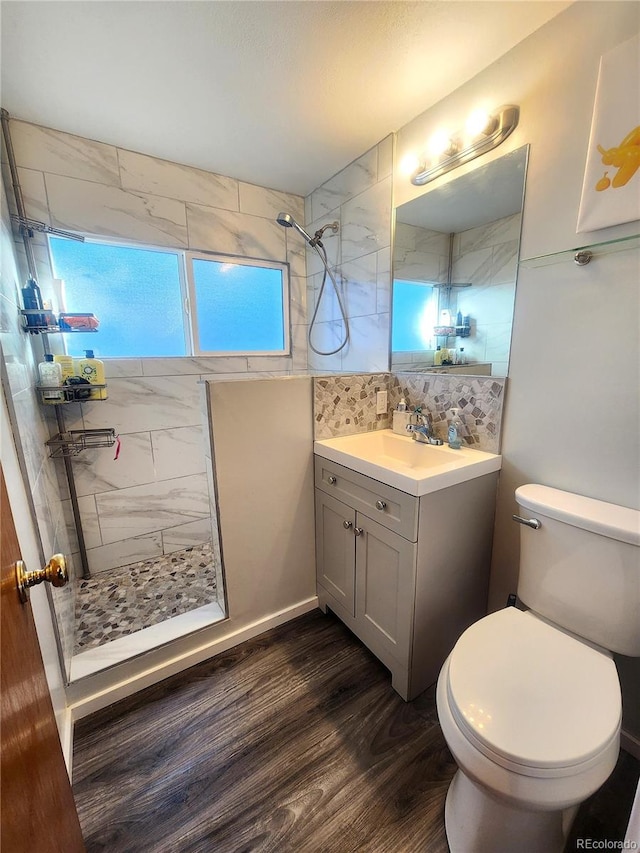 bathroom with a tile shower, hardwood / wood-style floors, toilet, decorative backsplash, and vanity