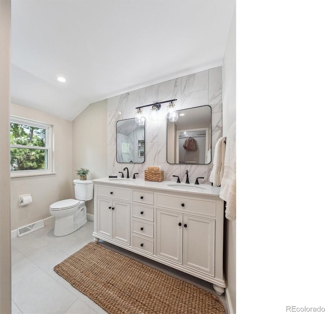 bathroom featuring toilet, baseboards, vaulted ceiling, double vanity, and tasteful backsplash
