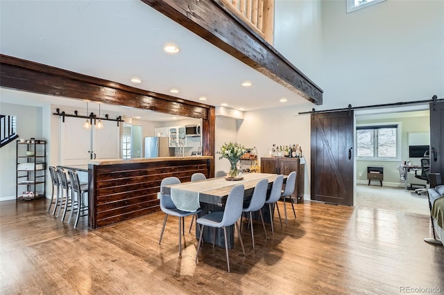 dining area with light hardwood / wood-style flooring, a barn door, a towering ceiling, and beam ceiling