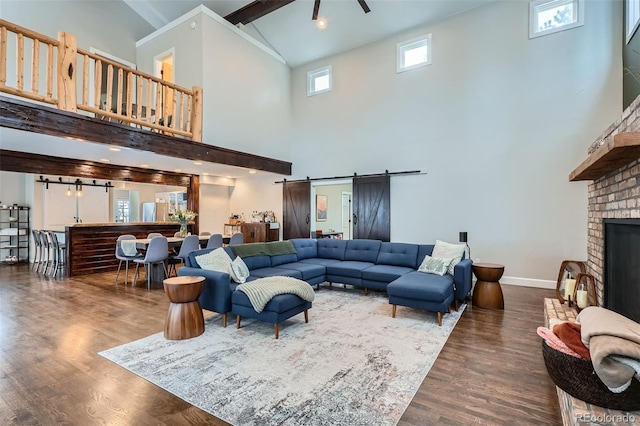 living room featuring dark hardwood / wood-style flooring, a barn door, a fireplace, high vaulted ceiling, and beam ceiling